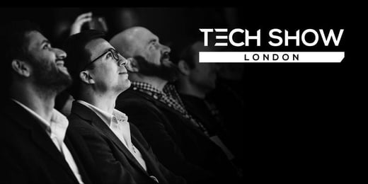 Tech Show London logo displayed on top of a black and white image of three people from the 2025 Mainstage crowd.